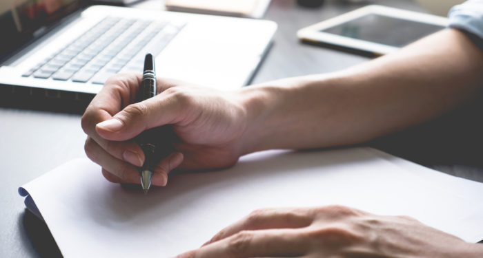 male hands writing on paper on his desk.